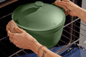 Person placing a green enameled cast iron pot into an oven using potholders