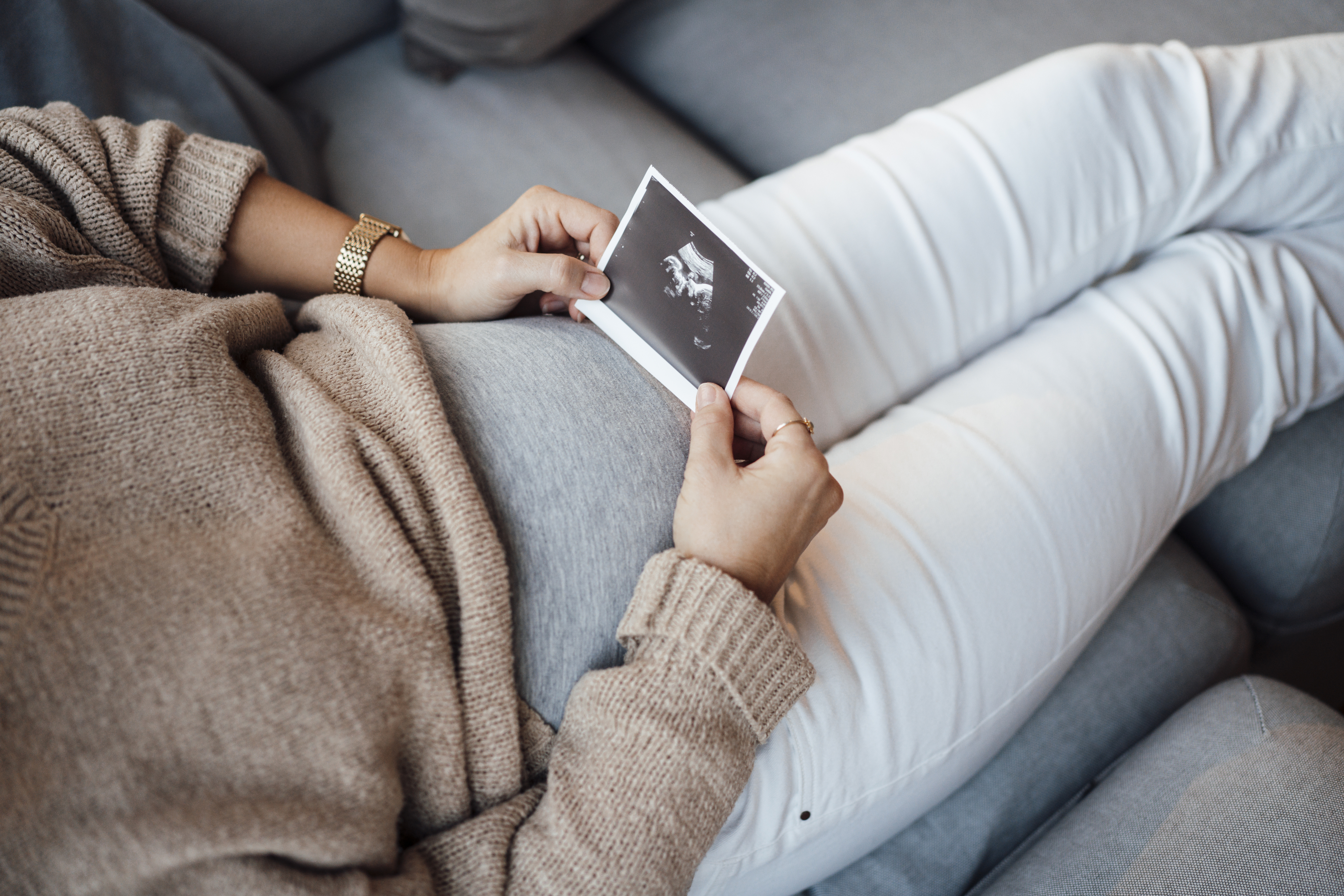 Pregnant person sitting, holding ultrasound photo over belly