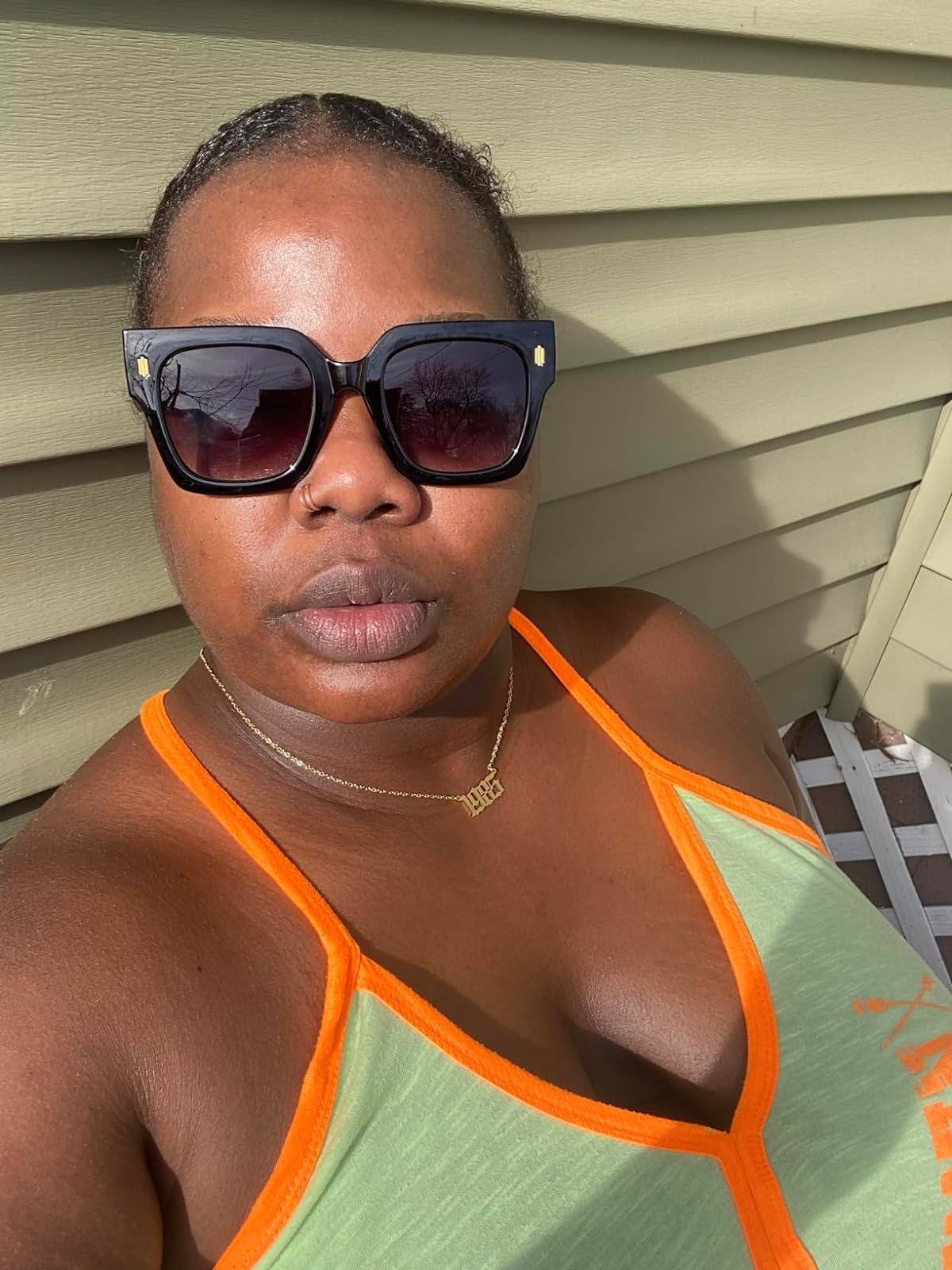 Reviewer in sunglasses and a green tank top with orange trim, taking a selfie in sunlight
