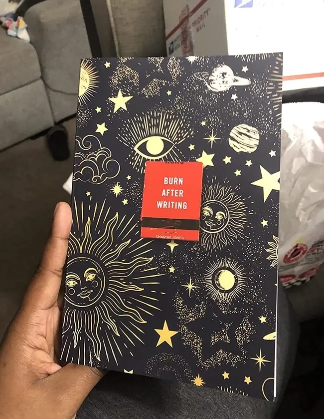 Person holding a book titled &quot;Burn After Writing&quot; with celestial designs on cover