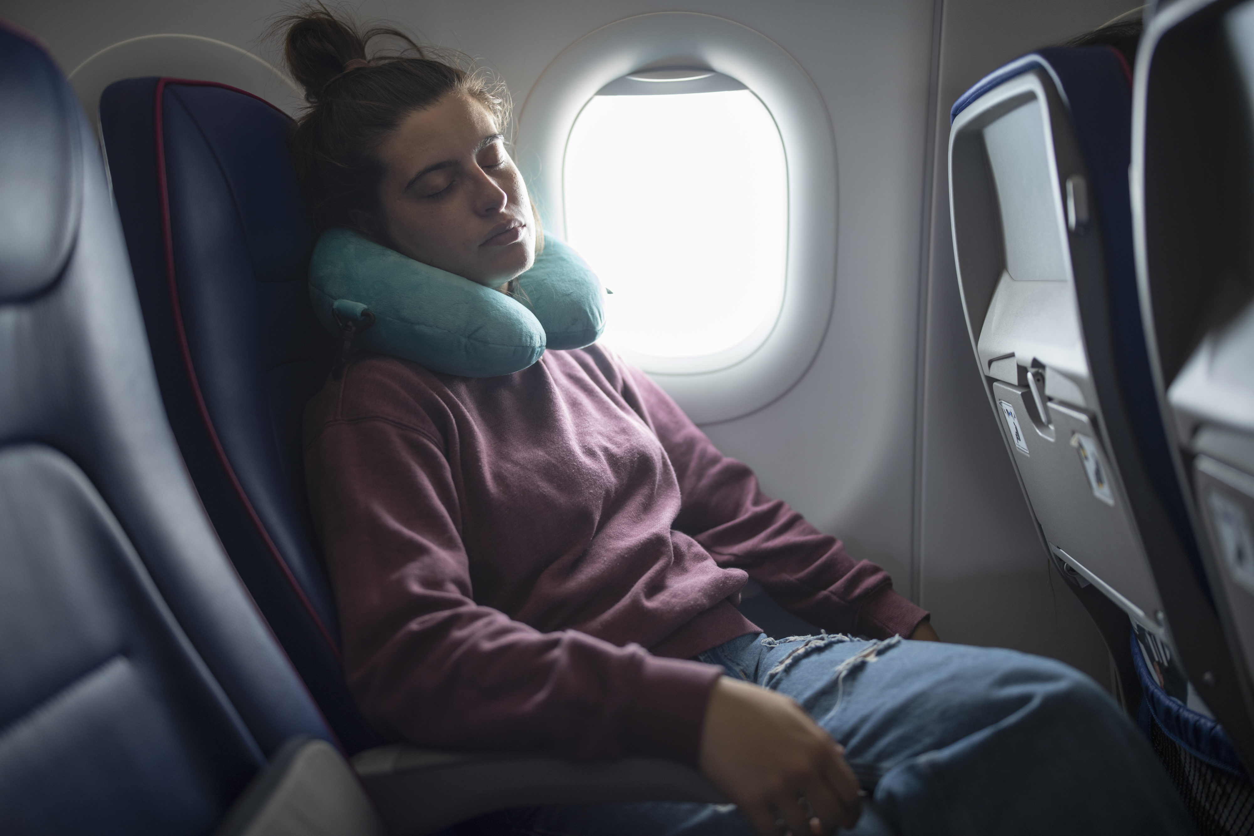Passenger asleep in an airplane seat with a neck pillow, signaling comfort during travel