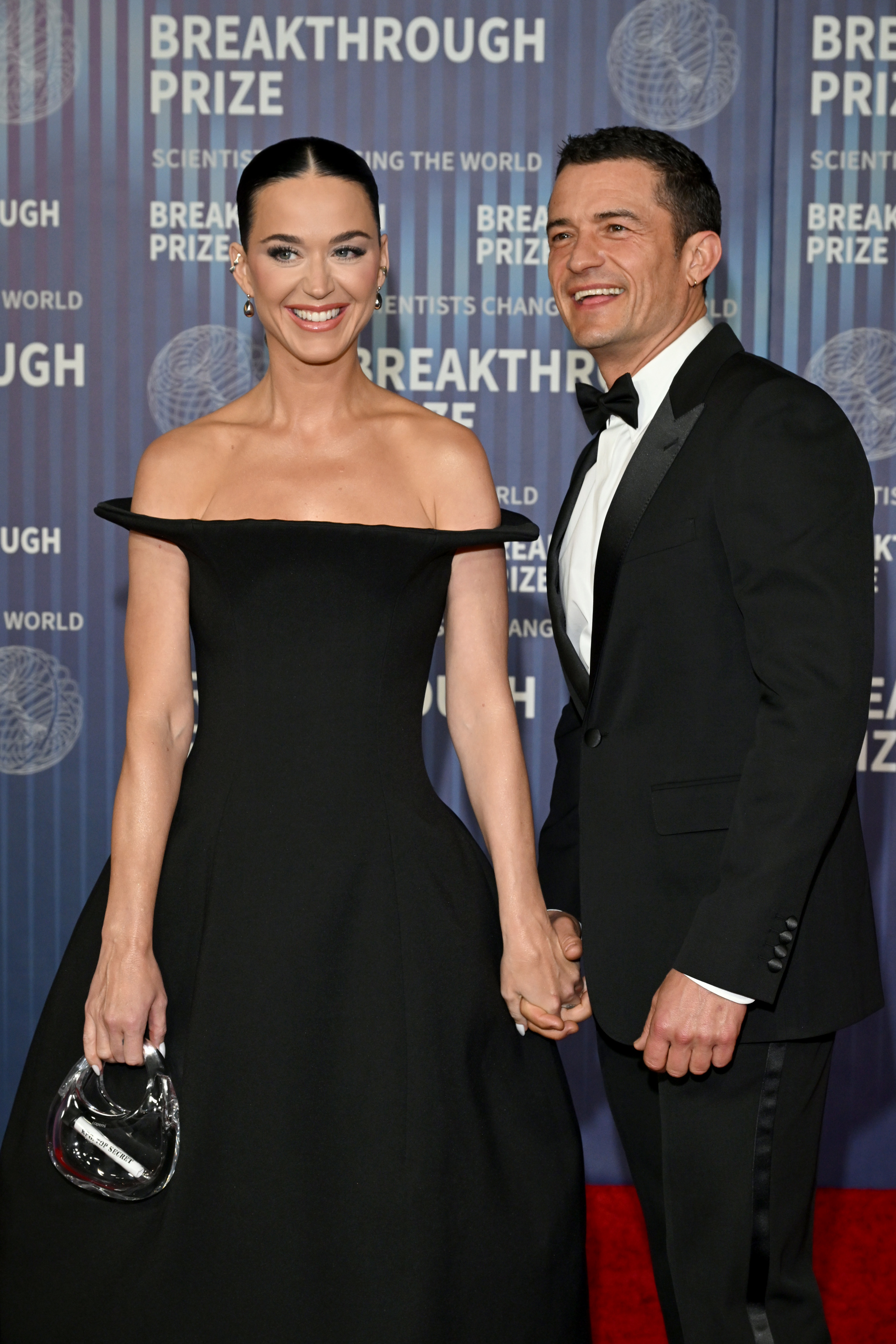 Closeup of Katy Perry and Orlando Bloom holding hands as they smile for photographers on the red carpet