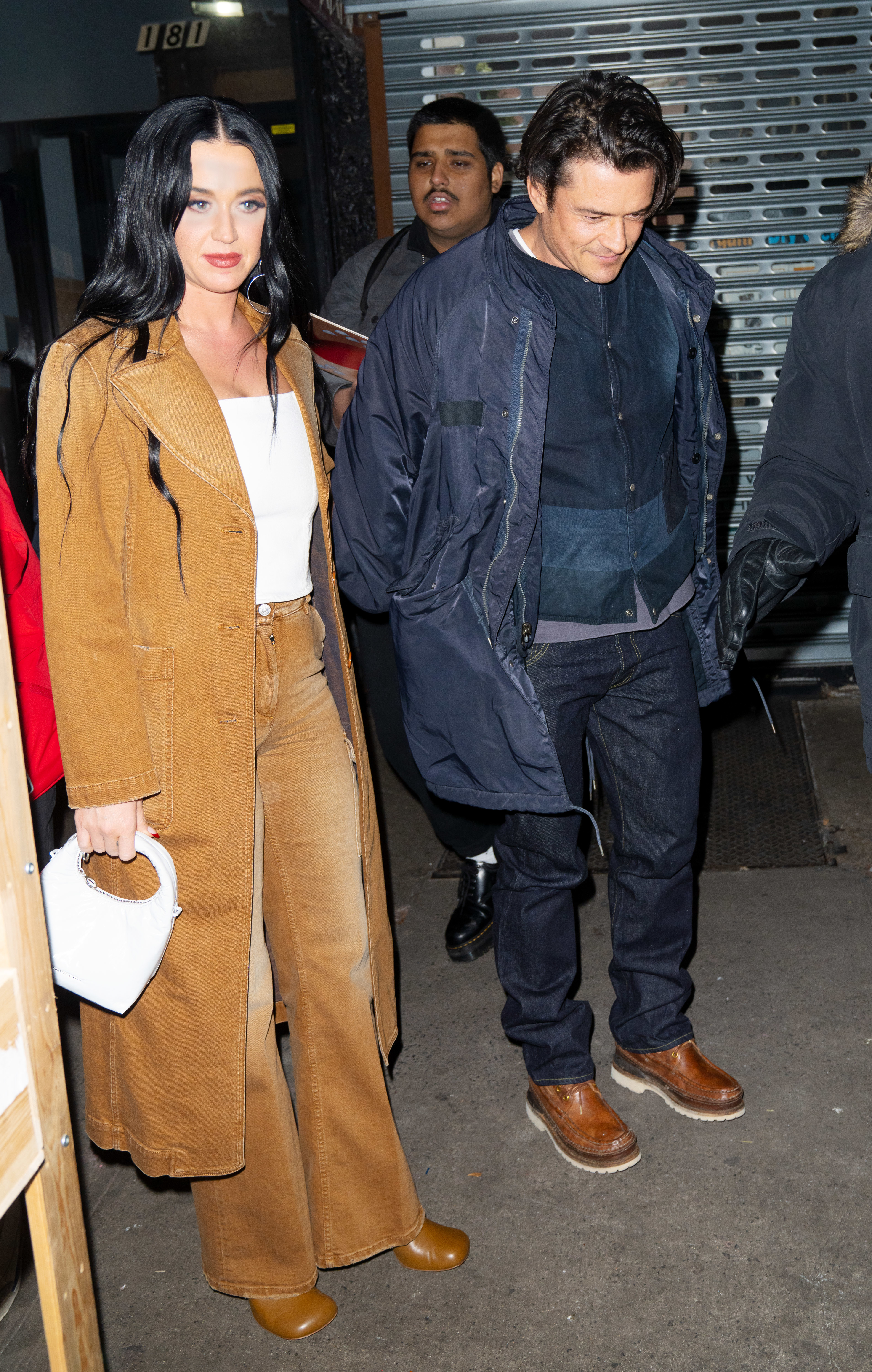 Katy Perry wears a long coat over a top and flared trousers as she walks with Orlando Bloom who&#x27;s wearing a casual jacket and jeans