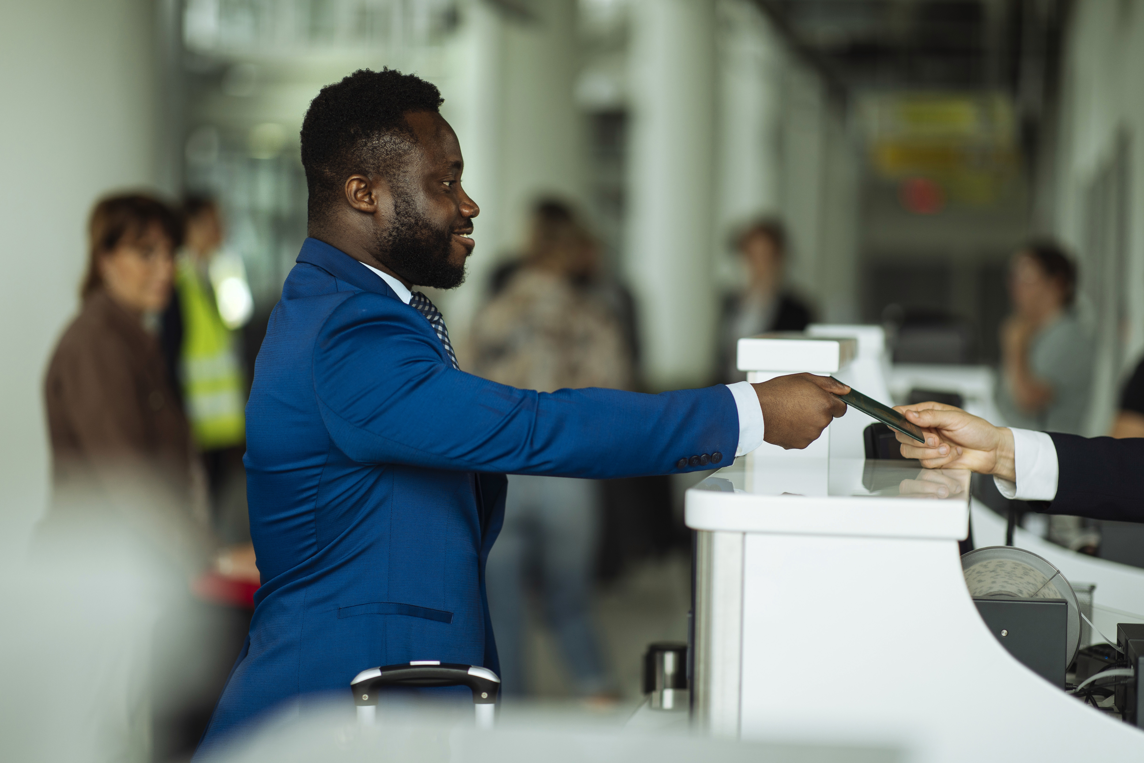 Man in suit handing over passport and boarding pass to airport staff at check-in counter