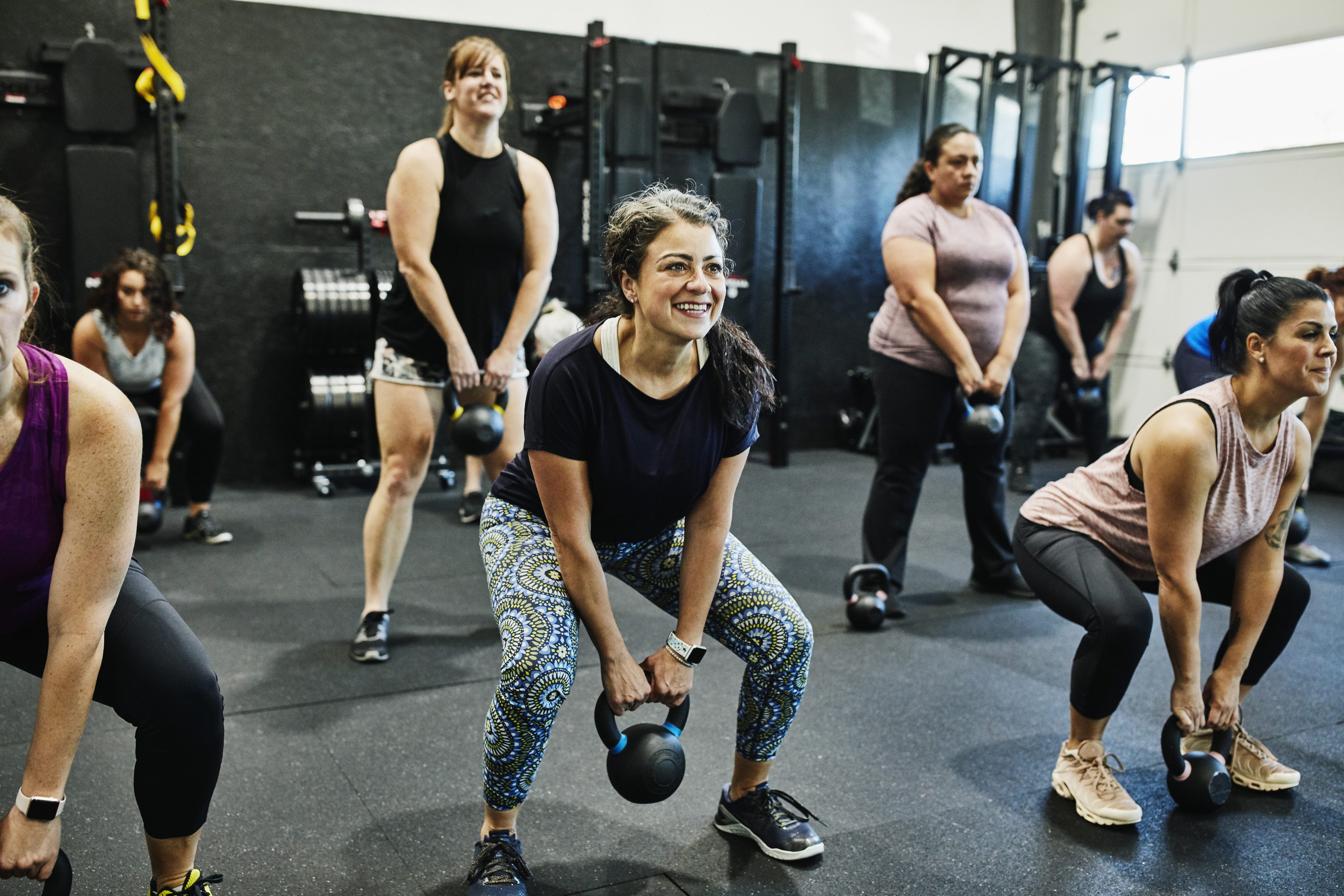 Group of people in a fitness class doing squats with kettlebells
