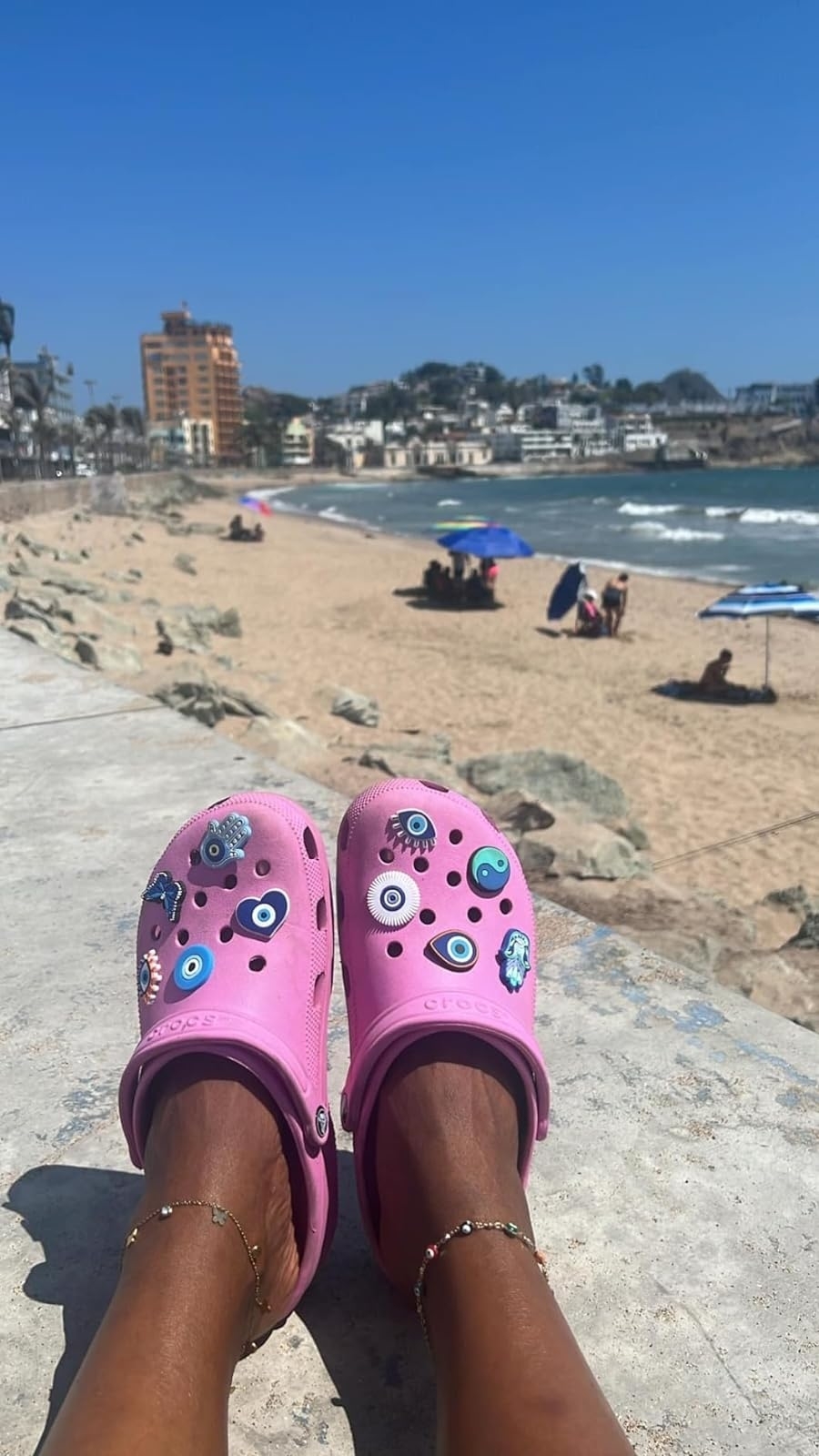 Person wearing embellished pink crocs by the beach