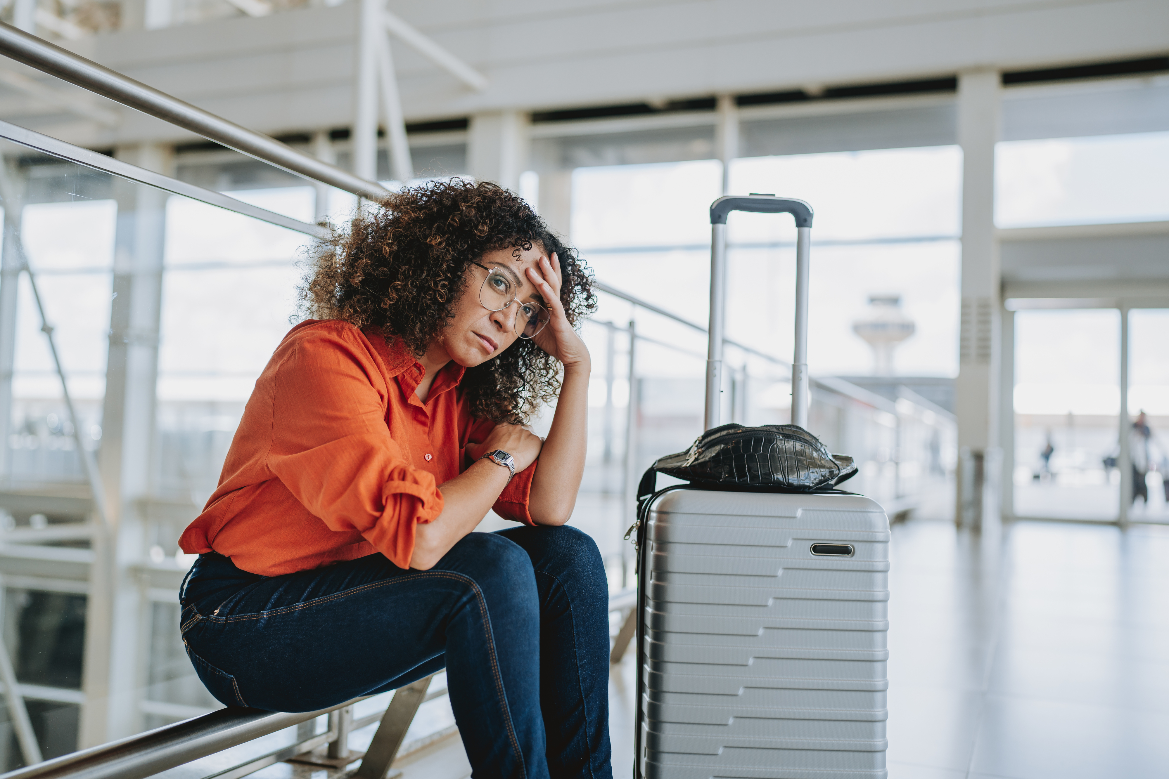 Woman sitting with suitcase in airport, looking distressed, possibly due to travel issues