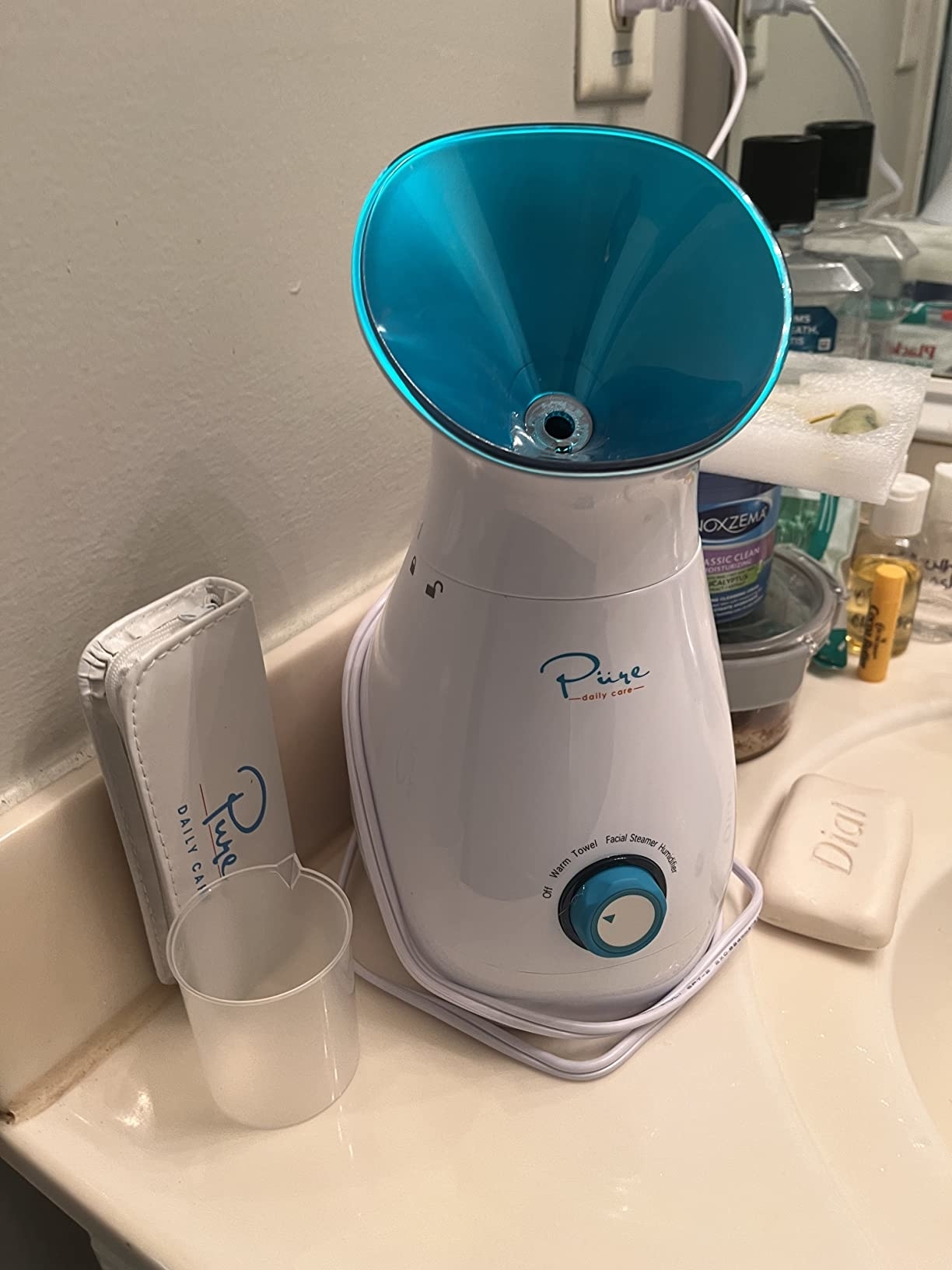 Facial steamer on a bathroom counter next to skincare products for home spa treatments