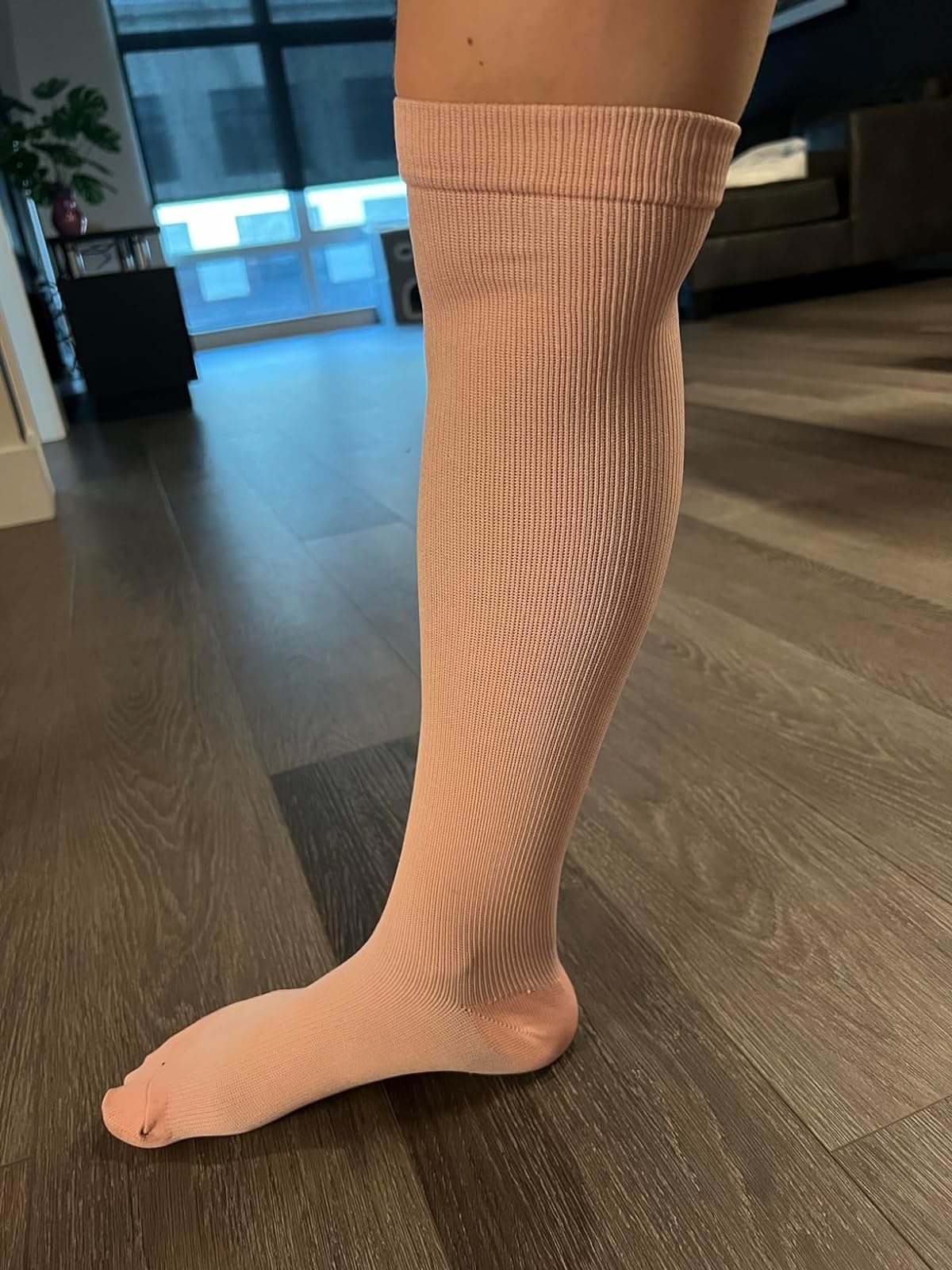 Close-up of a person wearing a single beige knee-high compression sock, standing on a wood floor