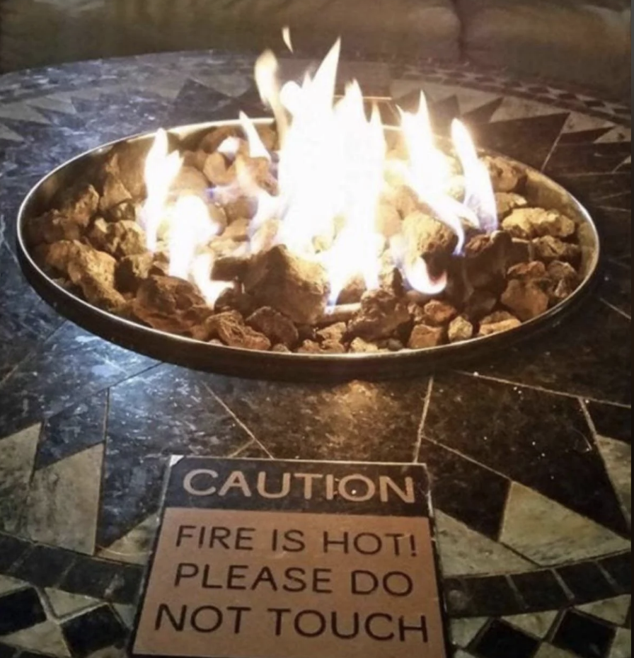 A fire pit with flames and a caution sign reading &quot;FIRE IS HOT! PLEASE DO NOT TOUCH&quot;