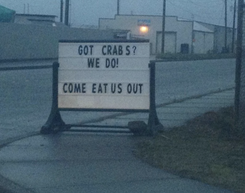 Roadside sign reads &quot;GOT CRAB S? WE DO! COME EAT US OUT,&quot; indicating a seafood offering with a spacing error