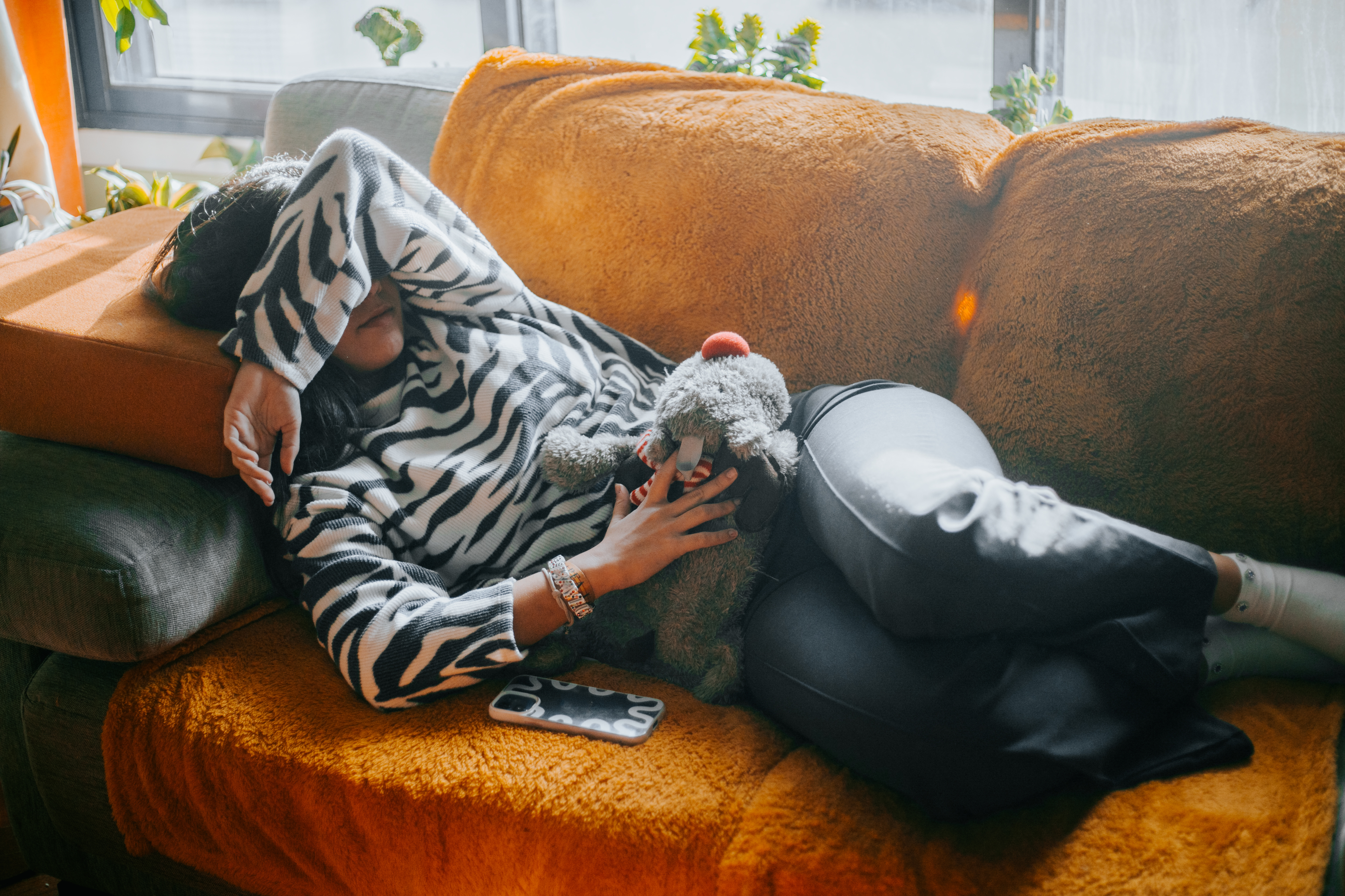 Person lounging on a couch in a zebra-stripe top and black pants, holding a grey stuffed animal