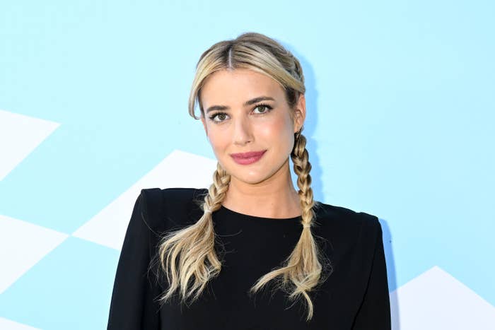 Emma Roberts in a dark outfit with her hair braided into pigtails at an event