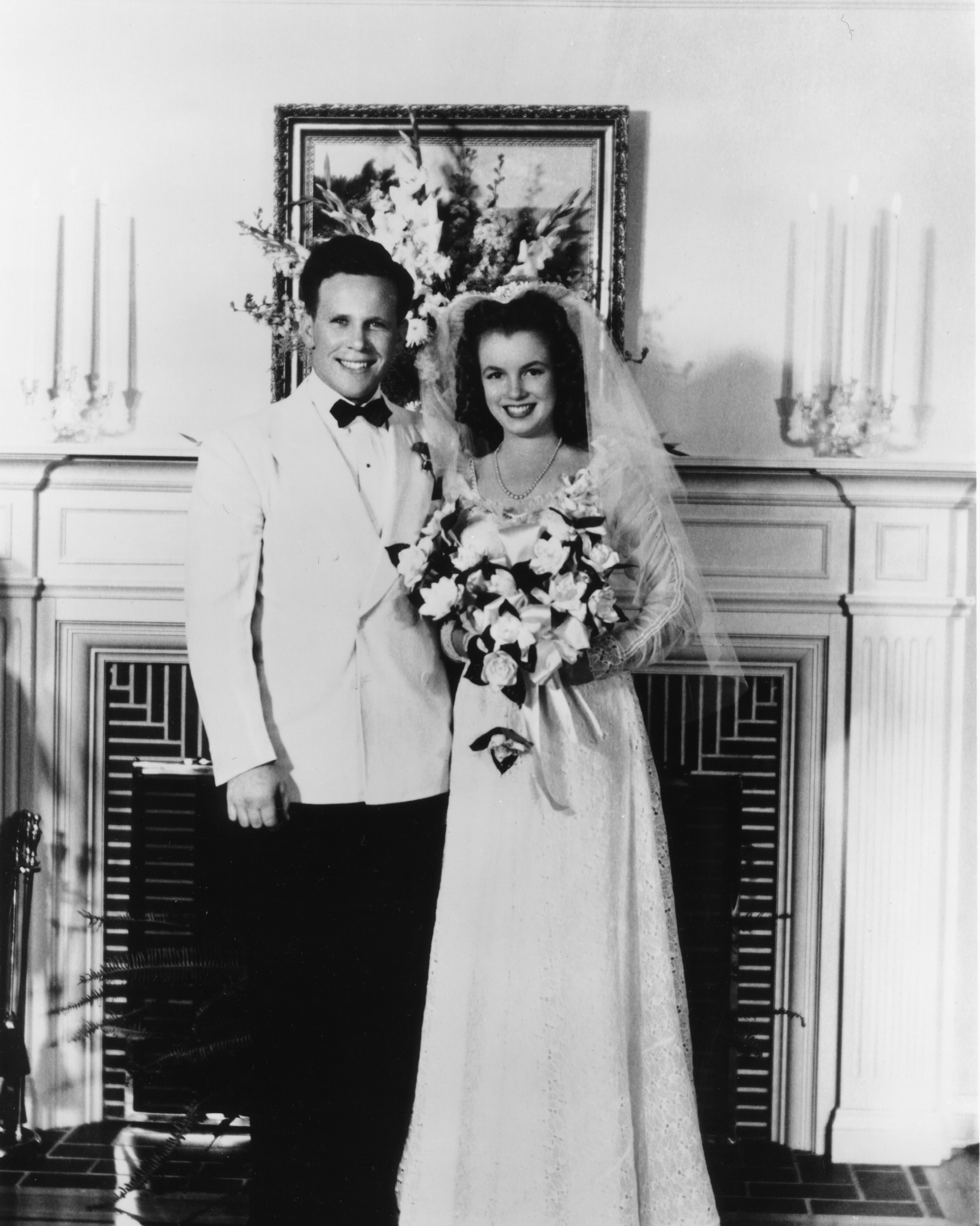 Bride in a long gown and groom in a tuxedo standing together, smiling at their wedding