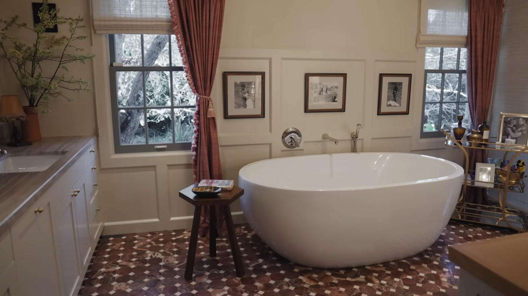 Elegant bathroom with a freestanding tub, framed art on walls, and a view of trees through windows
