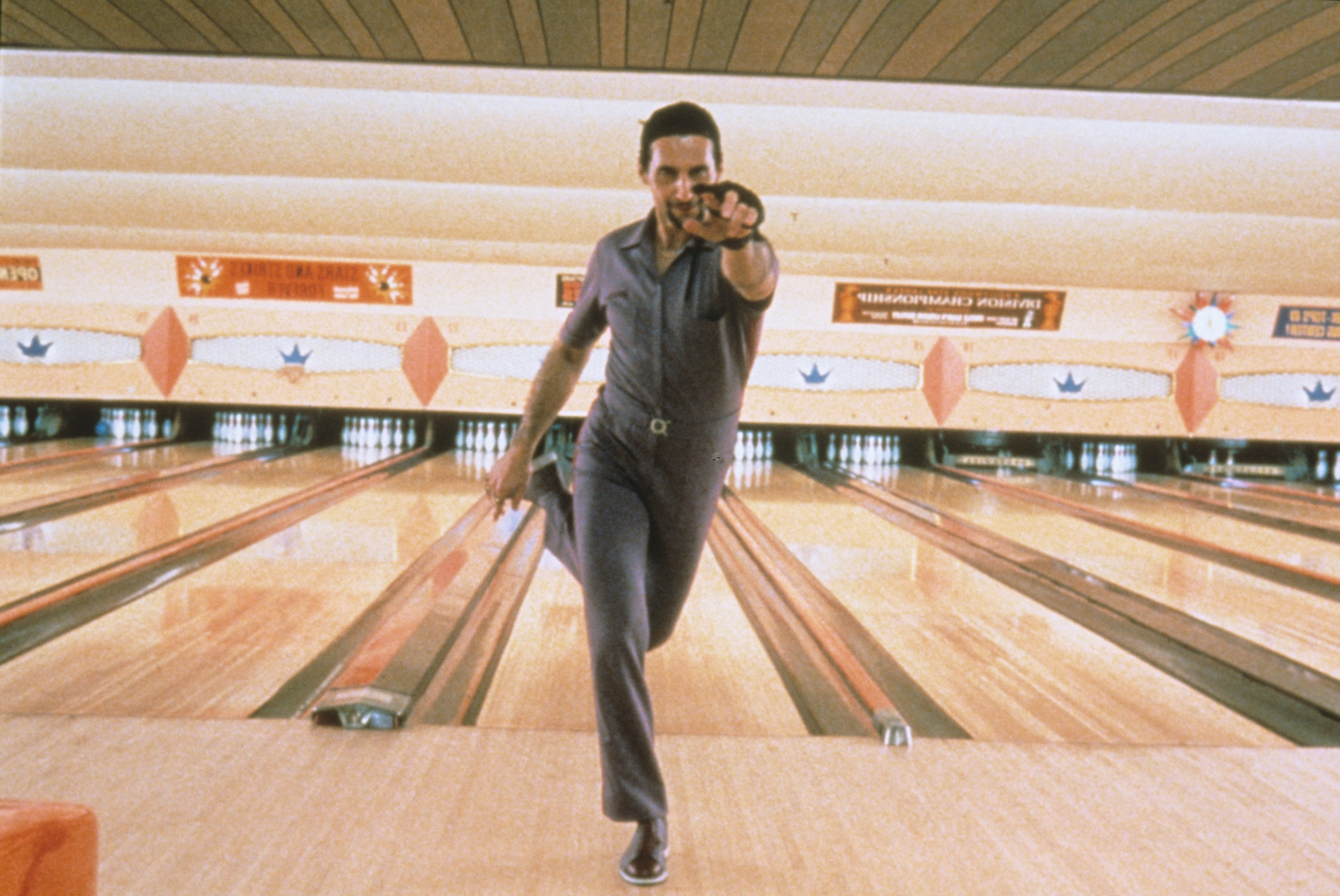 in a scene, John in a retro bowling shirt aims a bowling ball down the lane with intense focus
