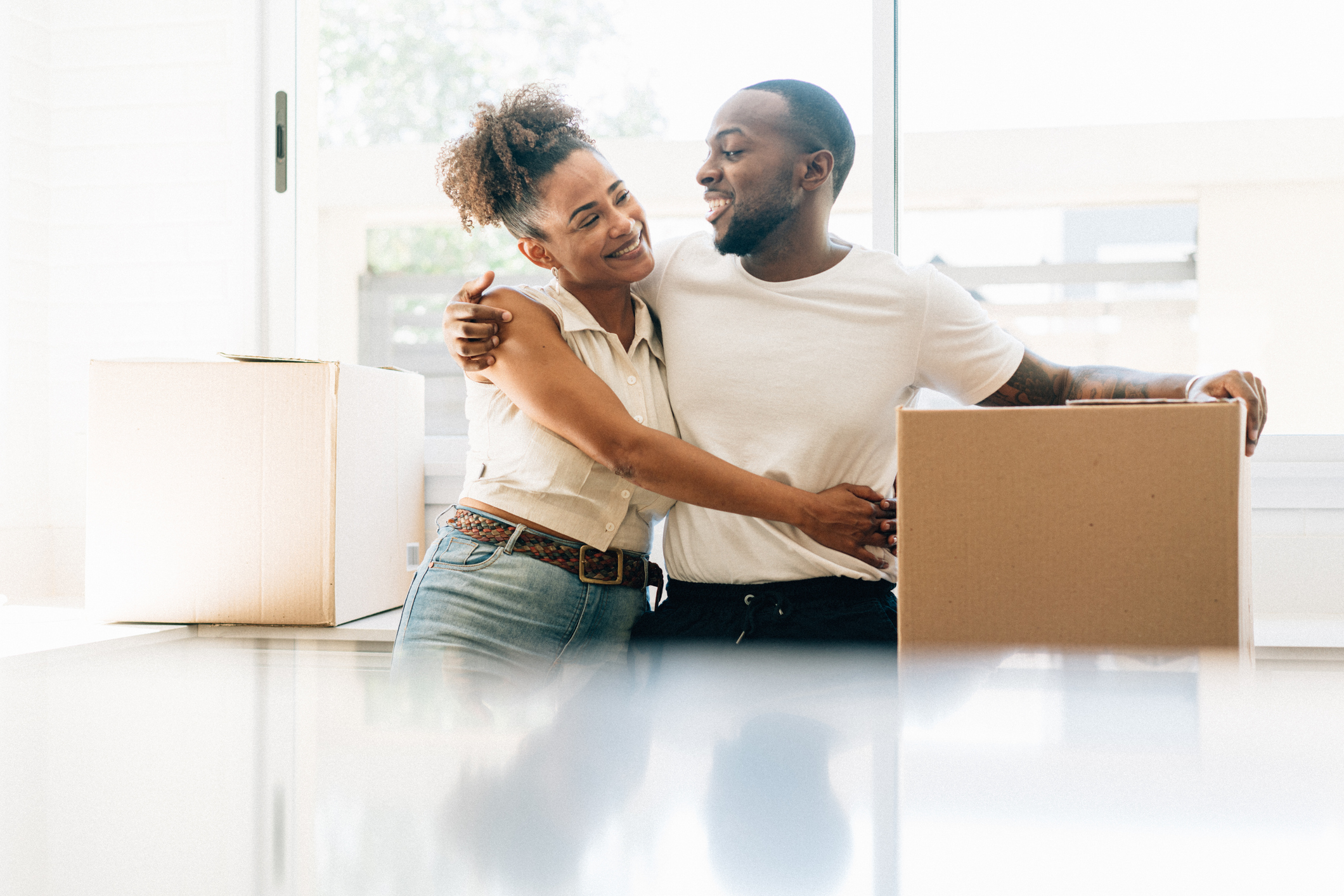 Couple embracing and smiling while sitting with a cardboard box suggesting moving in together