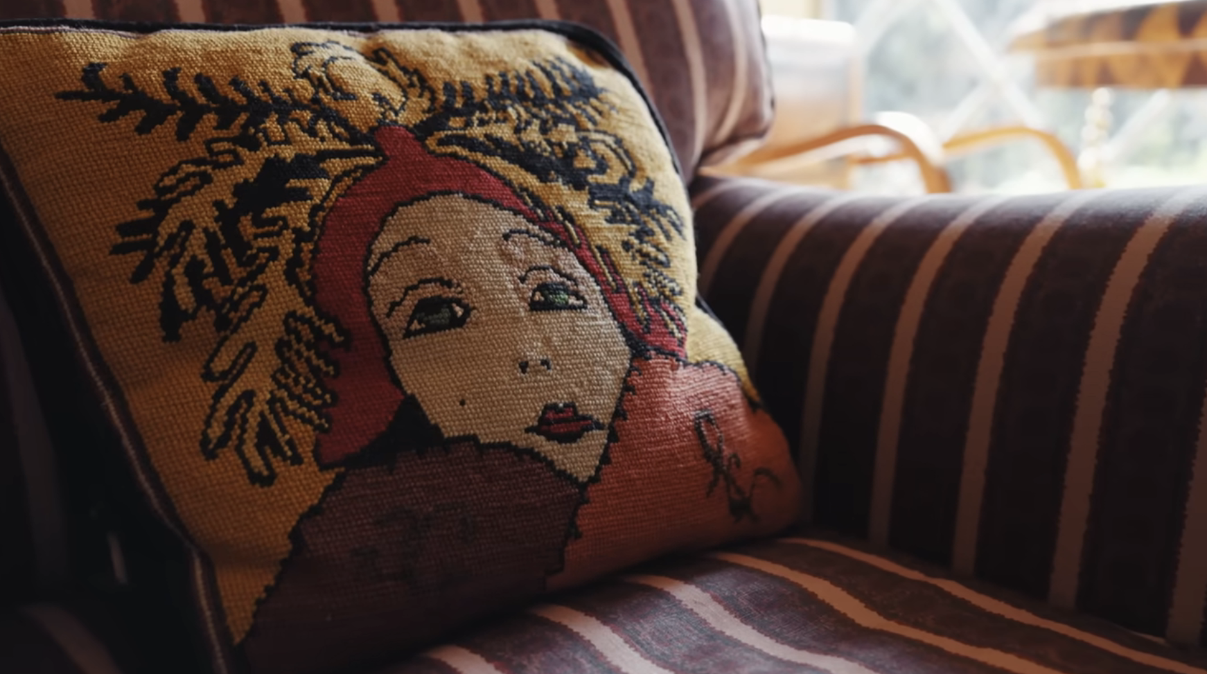 Embroidered cushion with a stylized female face on a striped sofa