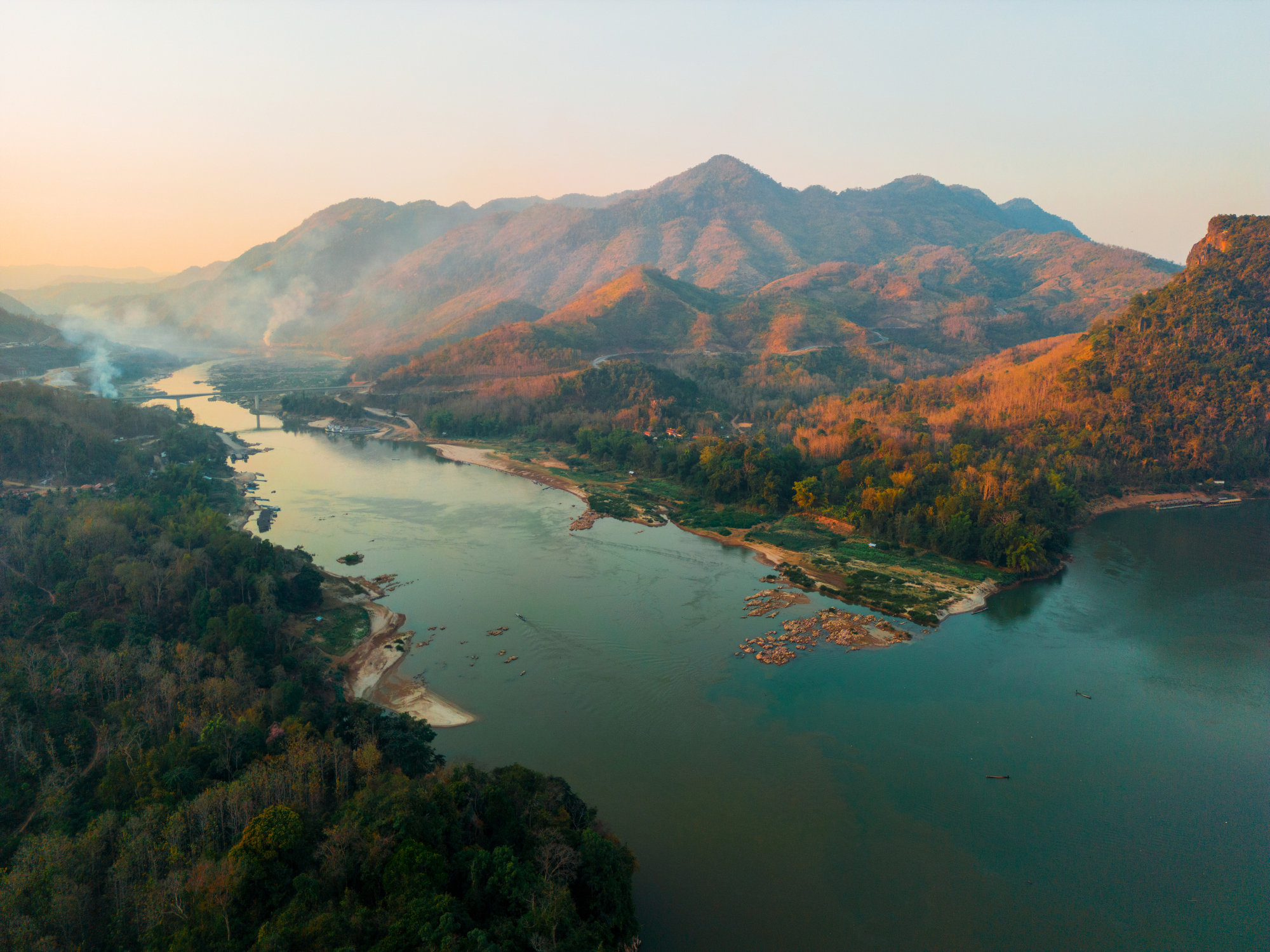 Aerial view of a winding river with adjacent forests and mountains during sunrise