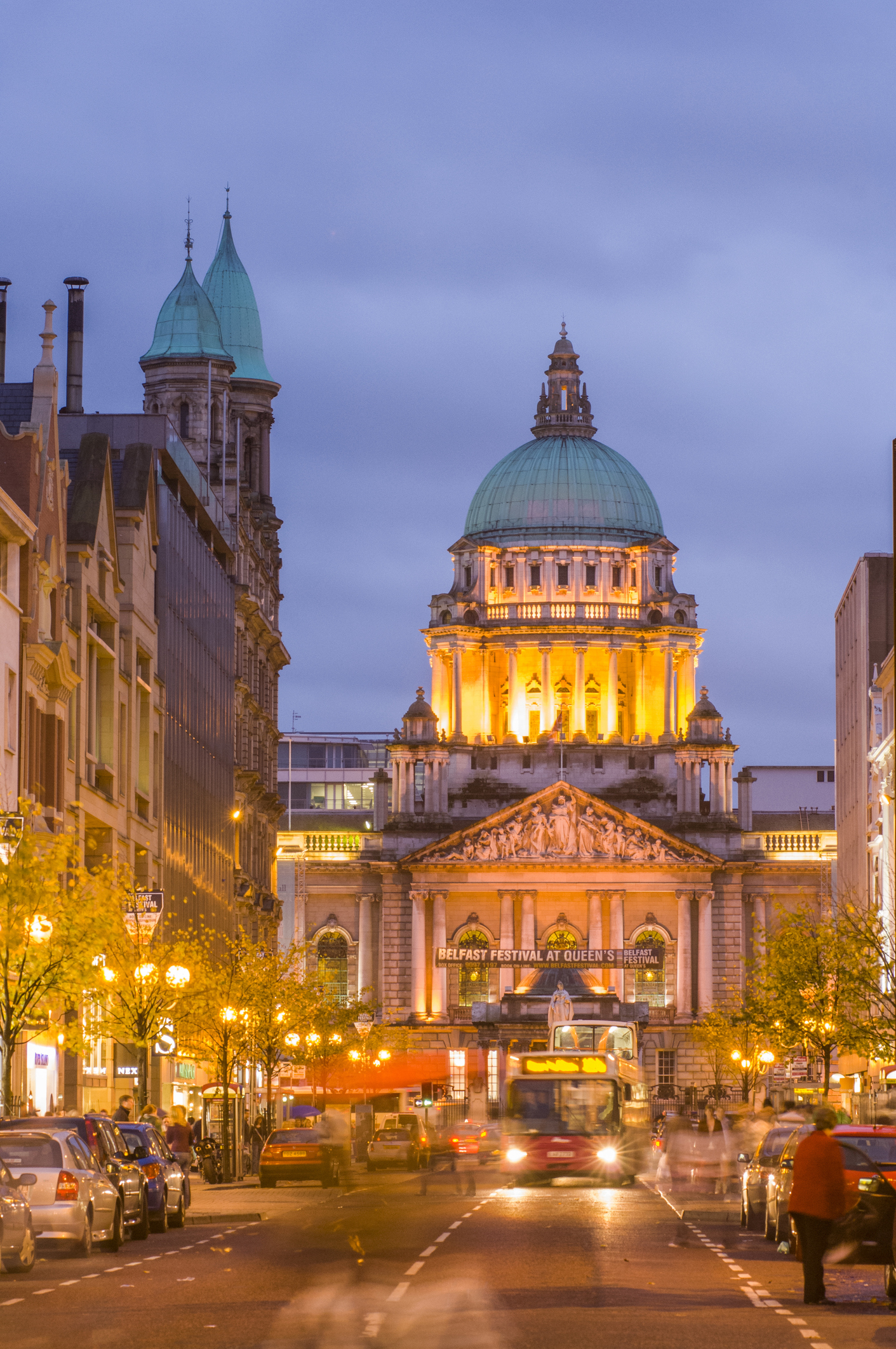 Evening view of Belfast City Hall illuminated, with busy street life and cars