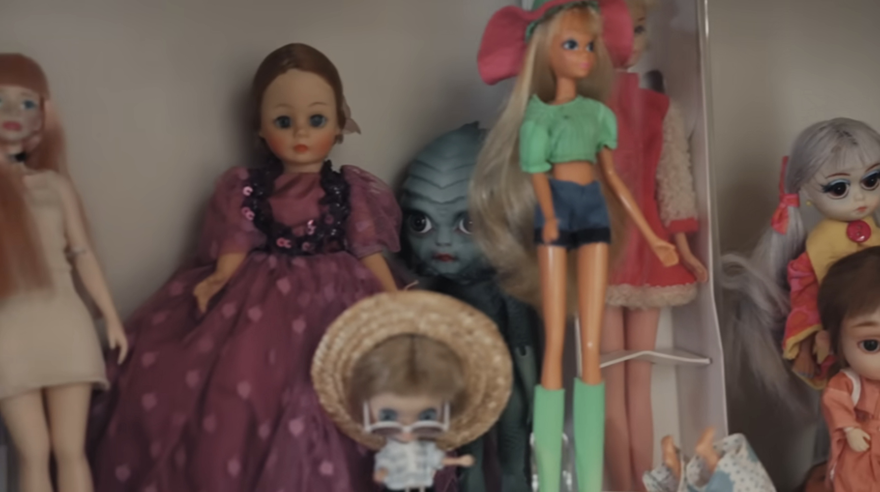 Assorted dolls of various styles on a shelf, including one with large eyes and another in a green top
