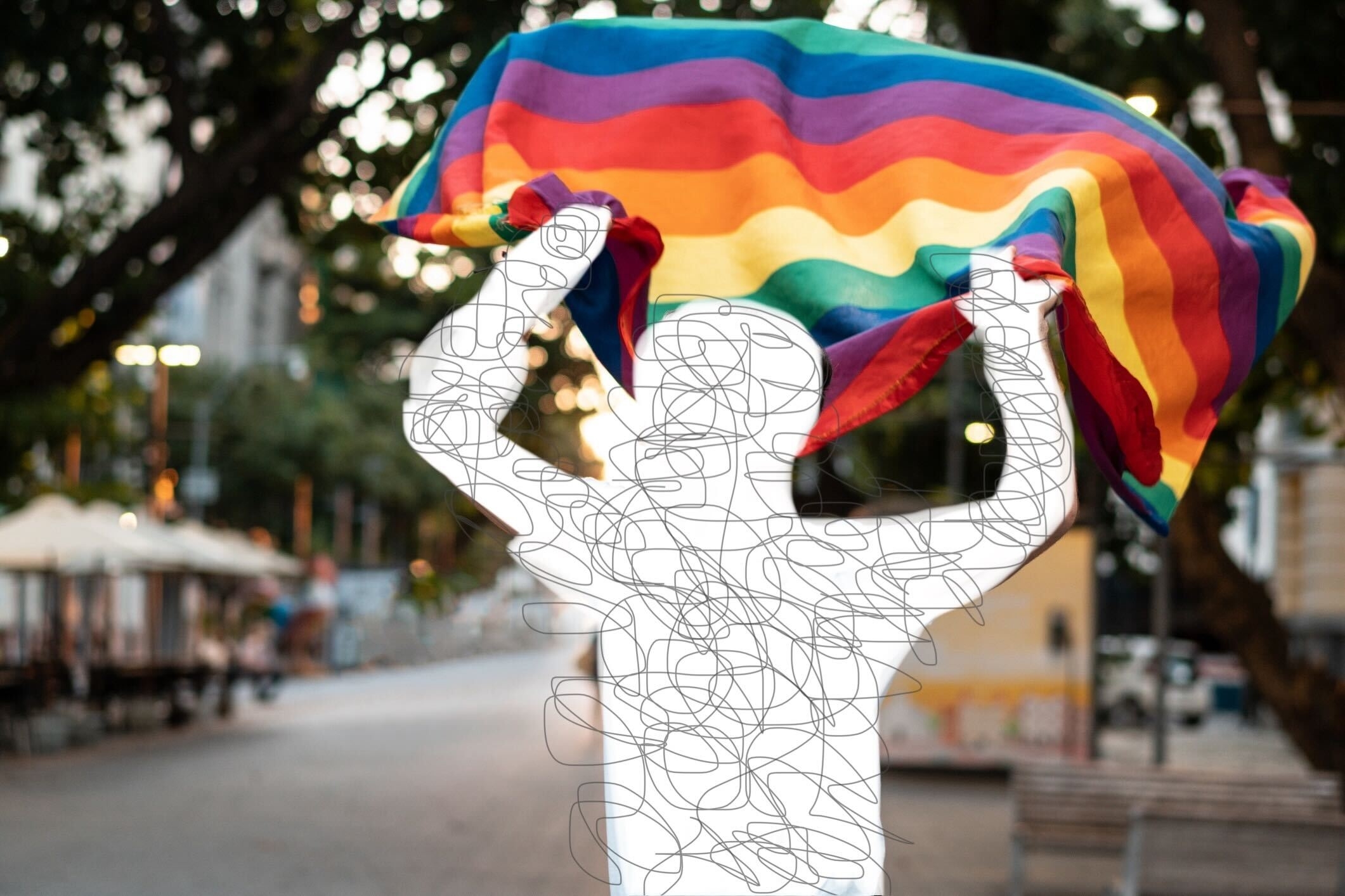 Person holds up a rainbow flag with their back to the camera in a street setting