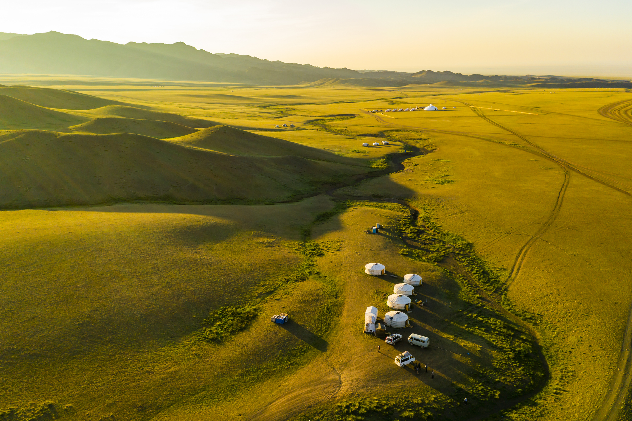 Aerial view of a cluster of traditional yurts in a vast grassy landscape at dawn or dusk
