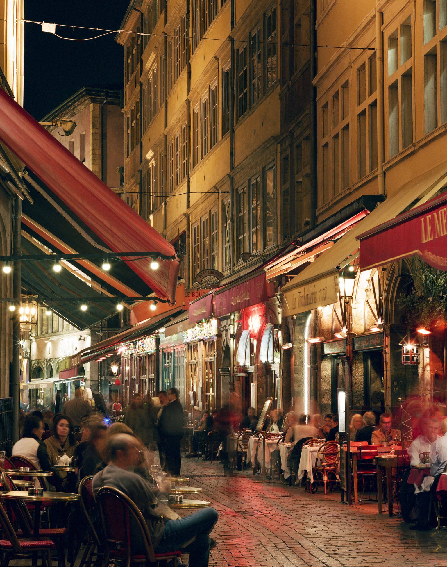 Outdoor dining scene at night with people at tables on a city street