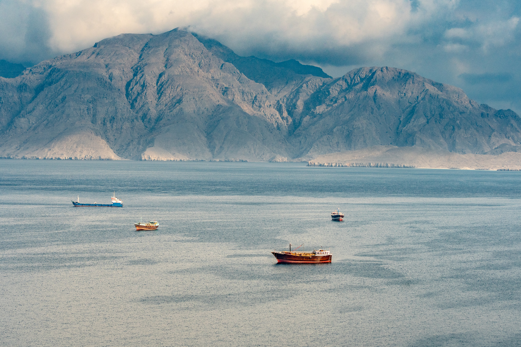 Boats on calm water with mountains in the background under overcast skies