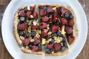 A sliced dessert pizza topped with raspberries, blueberries, and almonds on a white plate