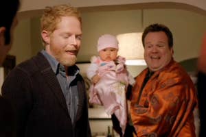 Cam from Modern Family holding baby Lily while Mitch stands to the side