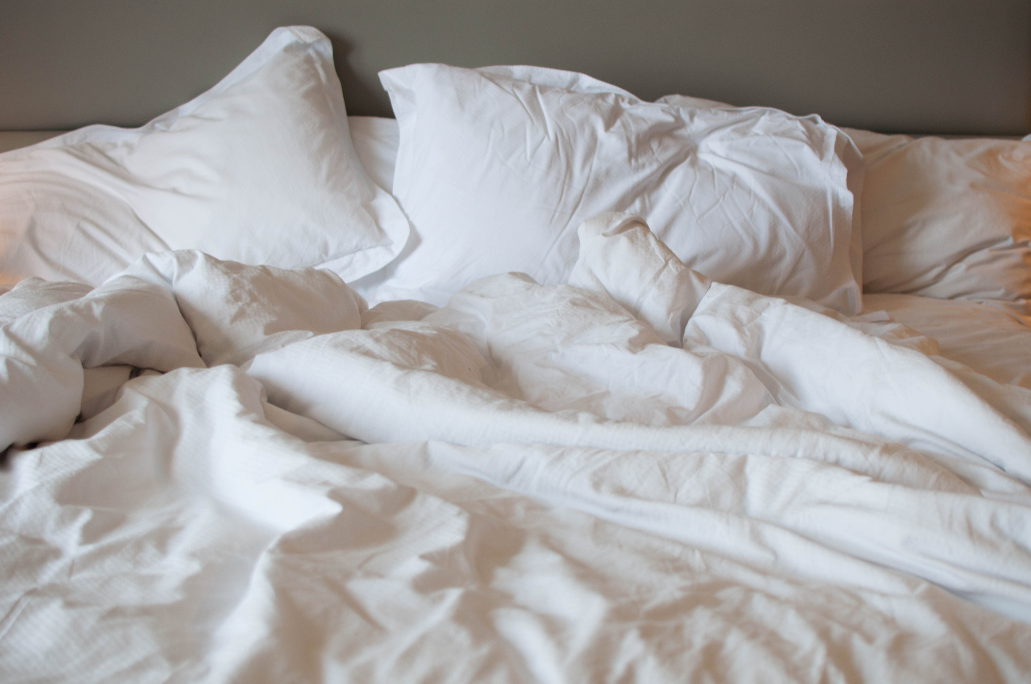 Unmade bed with rumpled white sheets and pillows, suggesting recent use