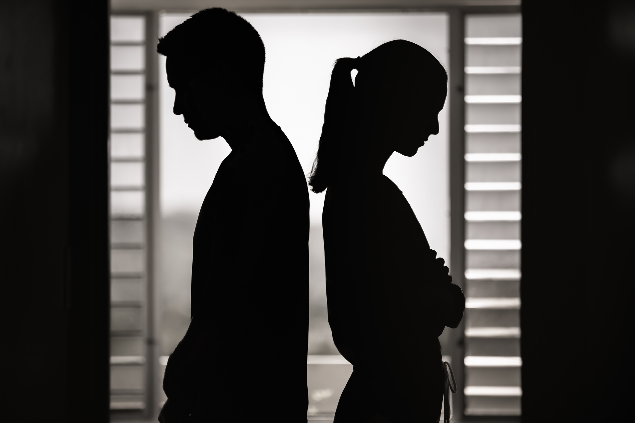 Silhouetted image of a man and woman facing away from each other with a tensioned posture
