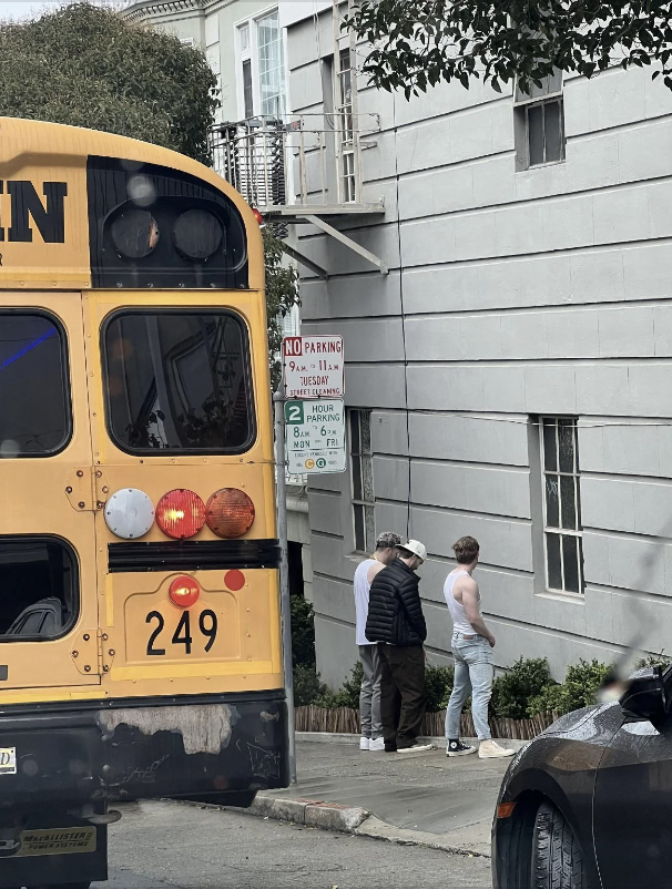 Three individuals standing by a No Parking sign next to a school bus, seemingly in discussion