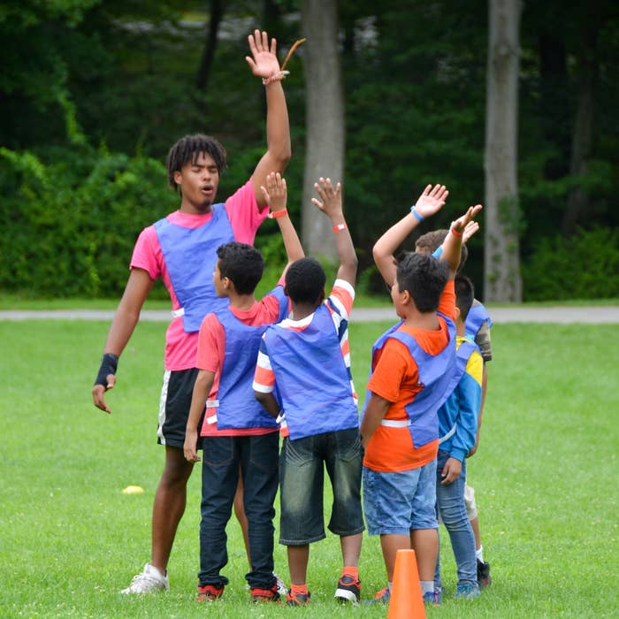 A group of children in brightly colored vests participate in an outdoor team activity, raising hands to answer a question