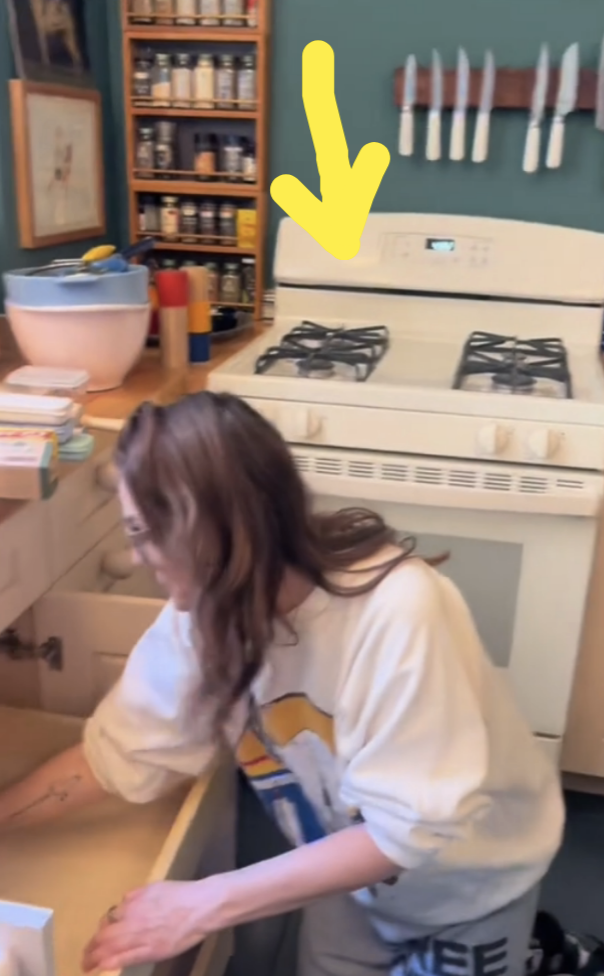 Drew  in a casual shirt doing kitchen work near a stove, with an arrow pointing at the stove
