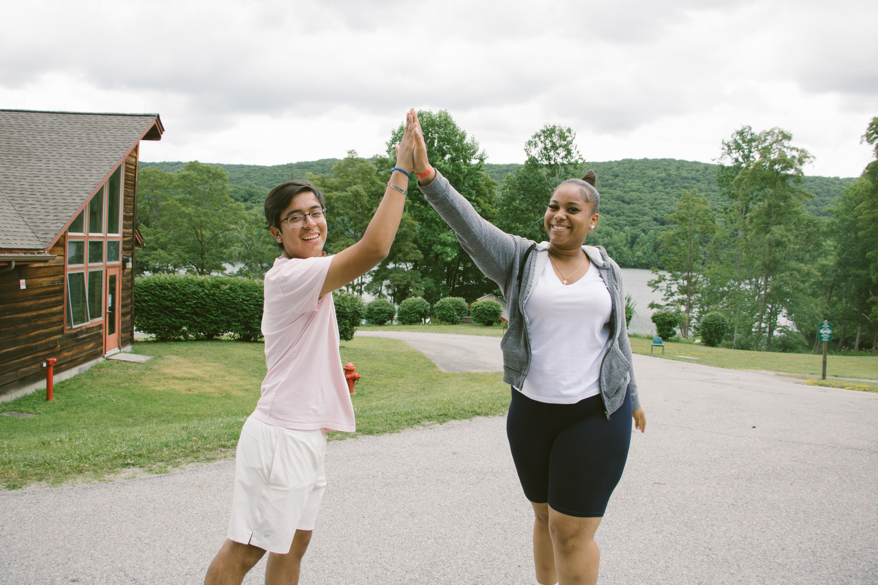 Two people high-fiving outdoors near buildings and trees