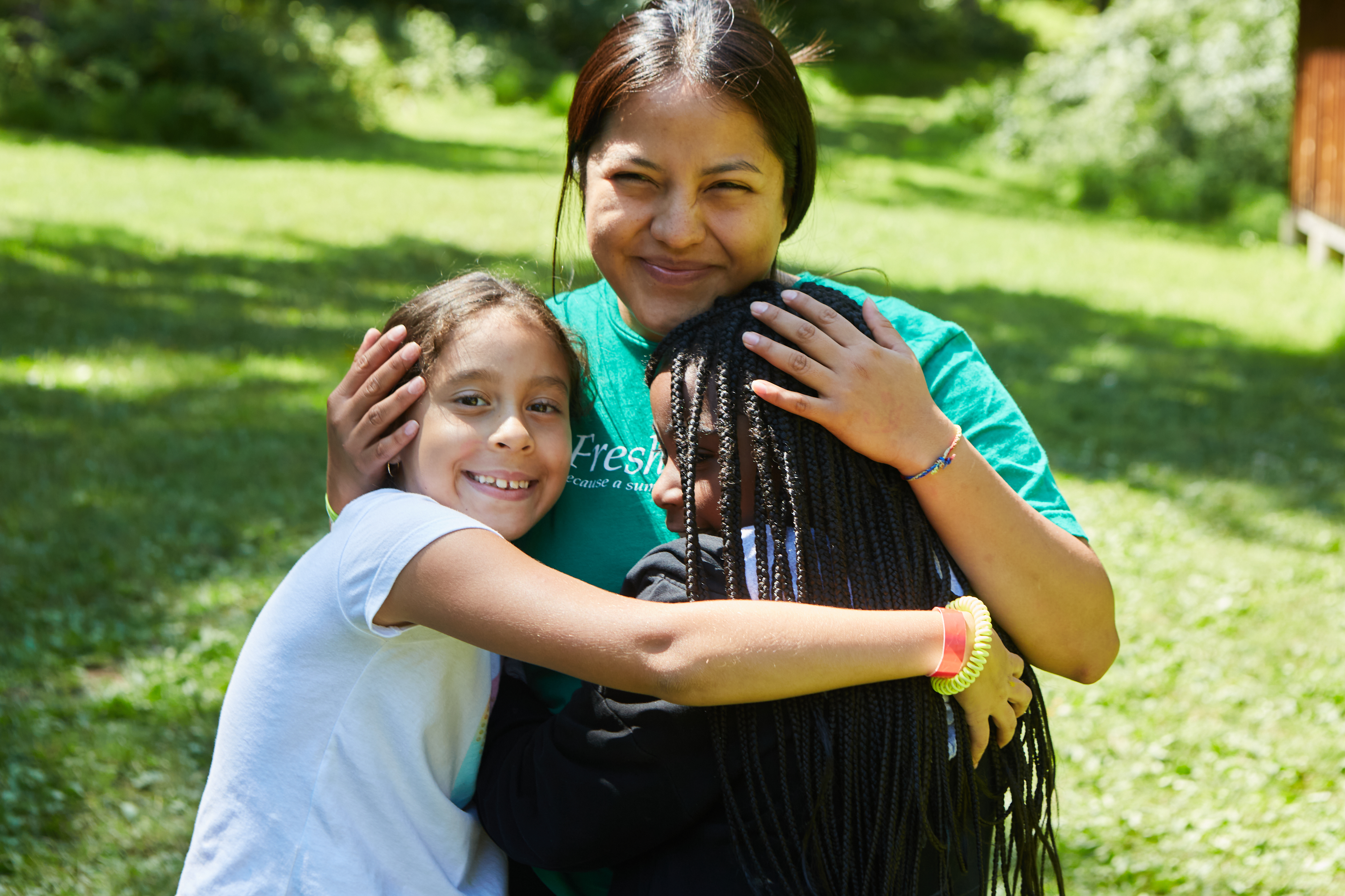 Two people smiling and hugging each other outside; they are wearing casual T-shirts