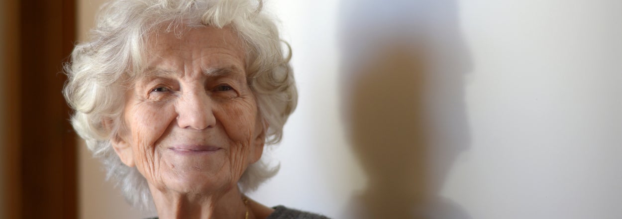 Elderly woman with a gentle smile wearing a casual sweater, with soft indoor lighting and shadow play on the wall