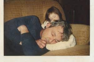 A child rests on a sleeping adult's back on a sofa, conveying a sense of familial comfort