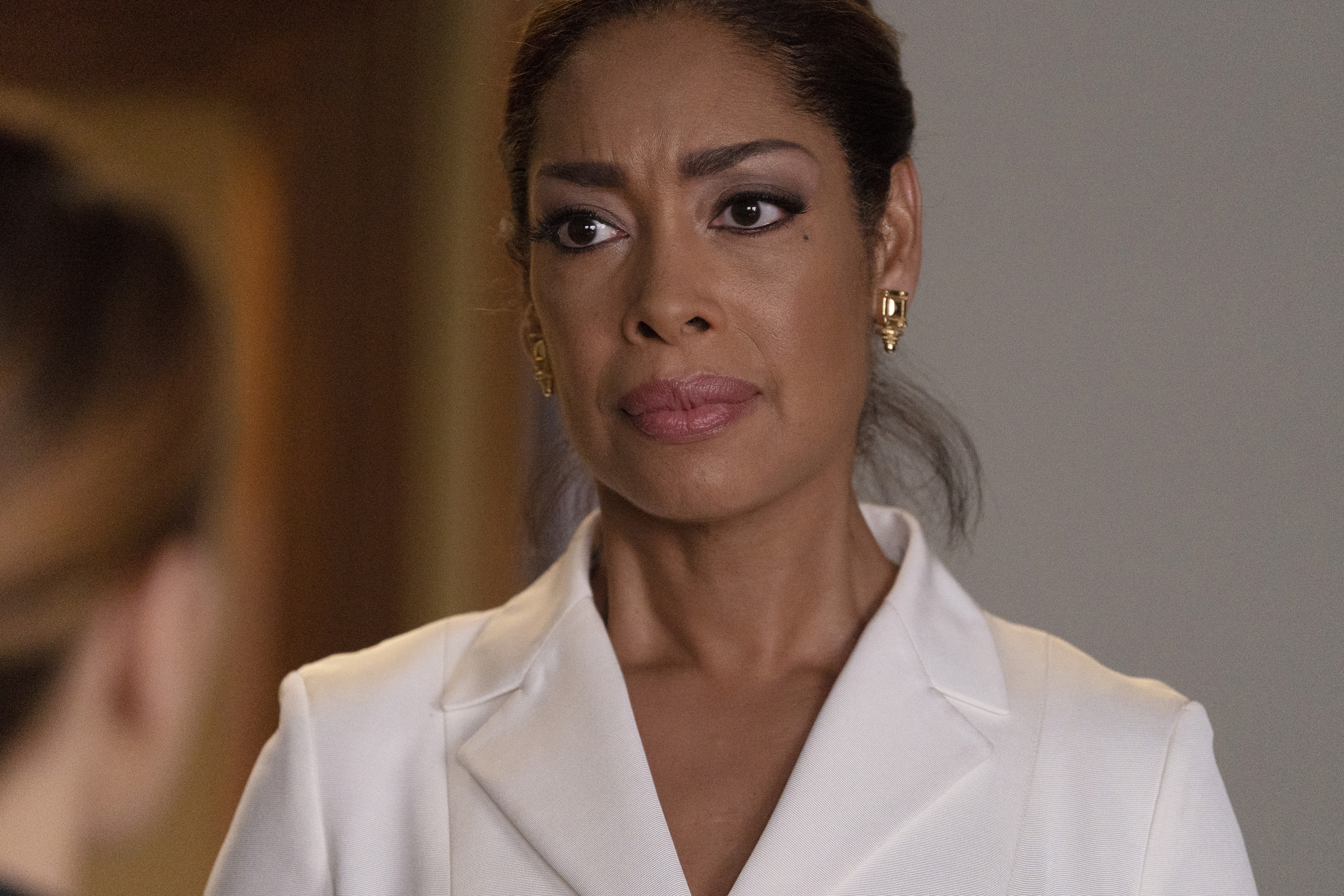 Gina Torres in a white blazer, looking concerned at someone out of frame