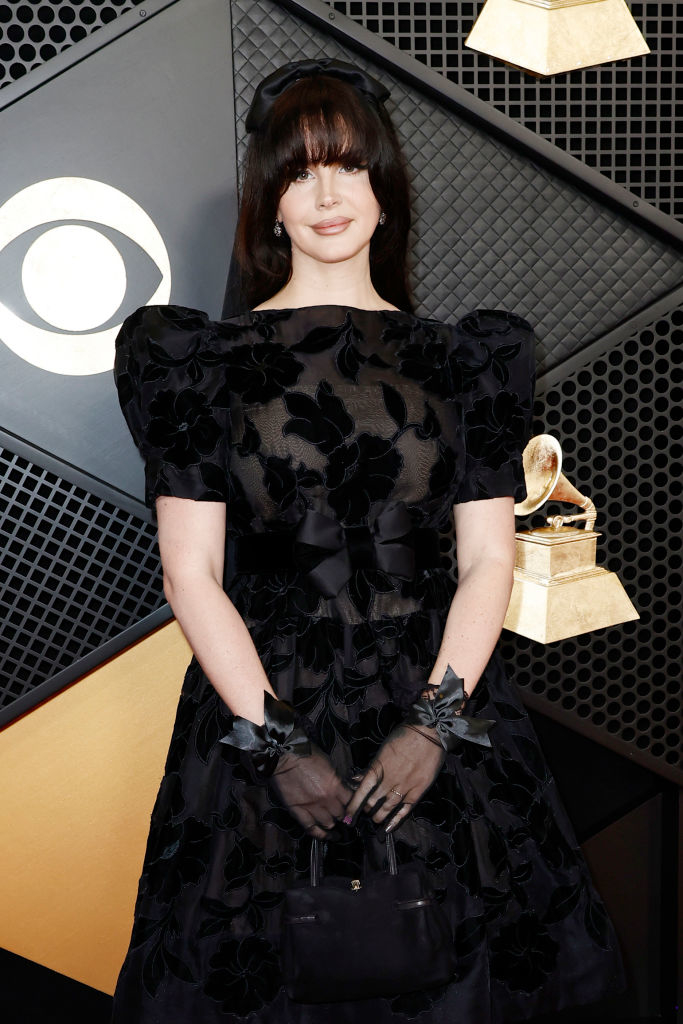 Lana on red carpet wearing a dress with ruffled details and holding a trophy