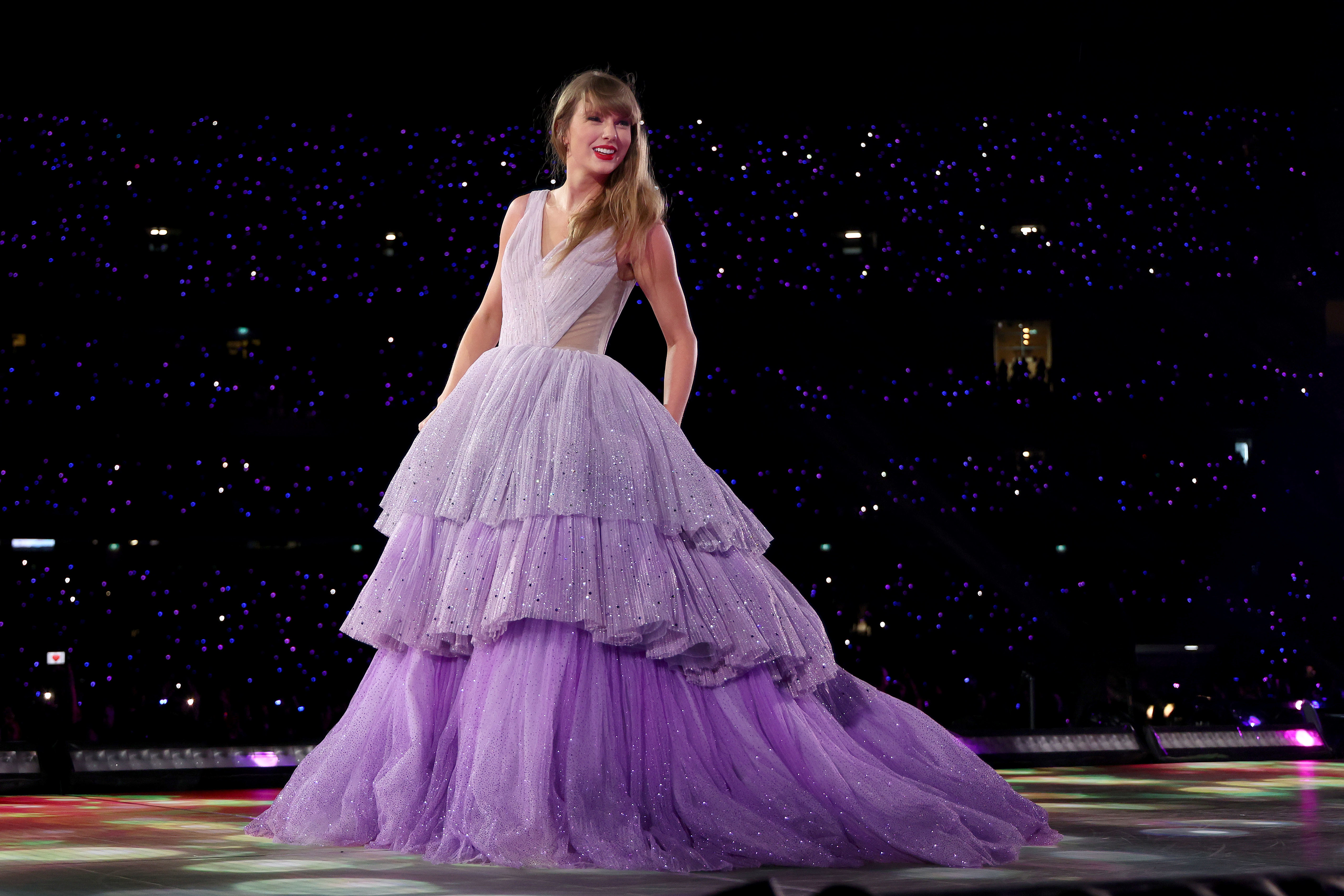 Taylor Swift in a layered gown at a night concert with sparkling background lights