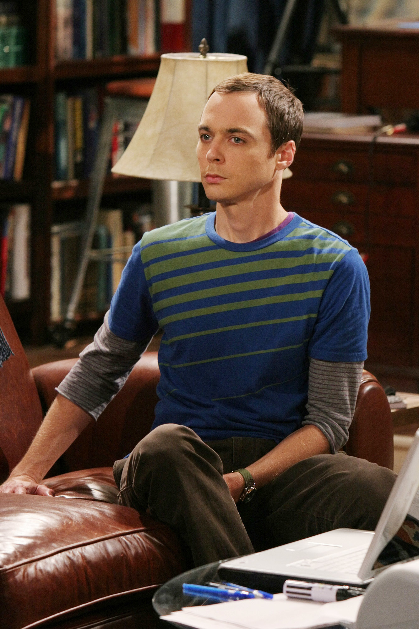 Sheldon Cooper from The Big Bang Theory sitting on a couch, wearing a striped long-sleeve shirt over a grey one