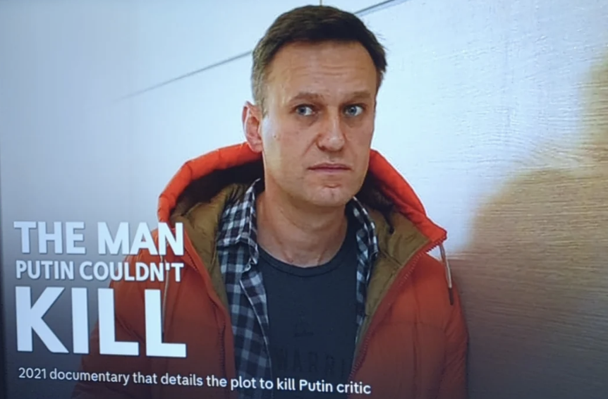 A man stands in front of a documentary title &quot;The Man Putin Couldn&#x27;t Kill&quot; summarizing a plot against Putin critic