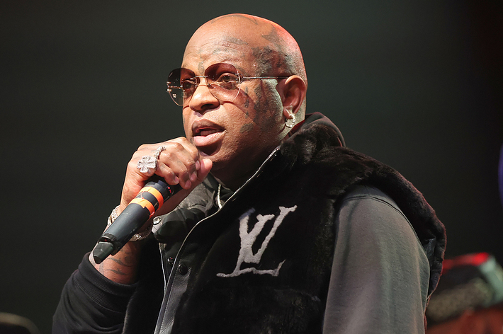 Music artist performing on stage with a microphone, wearing a logo sweater and glasses