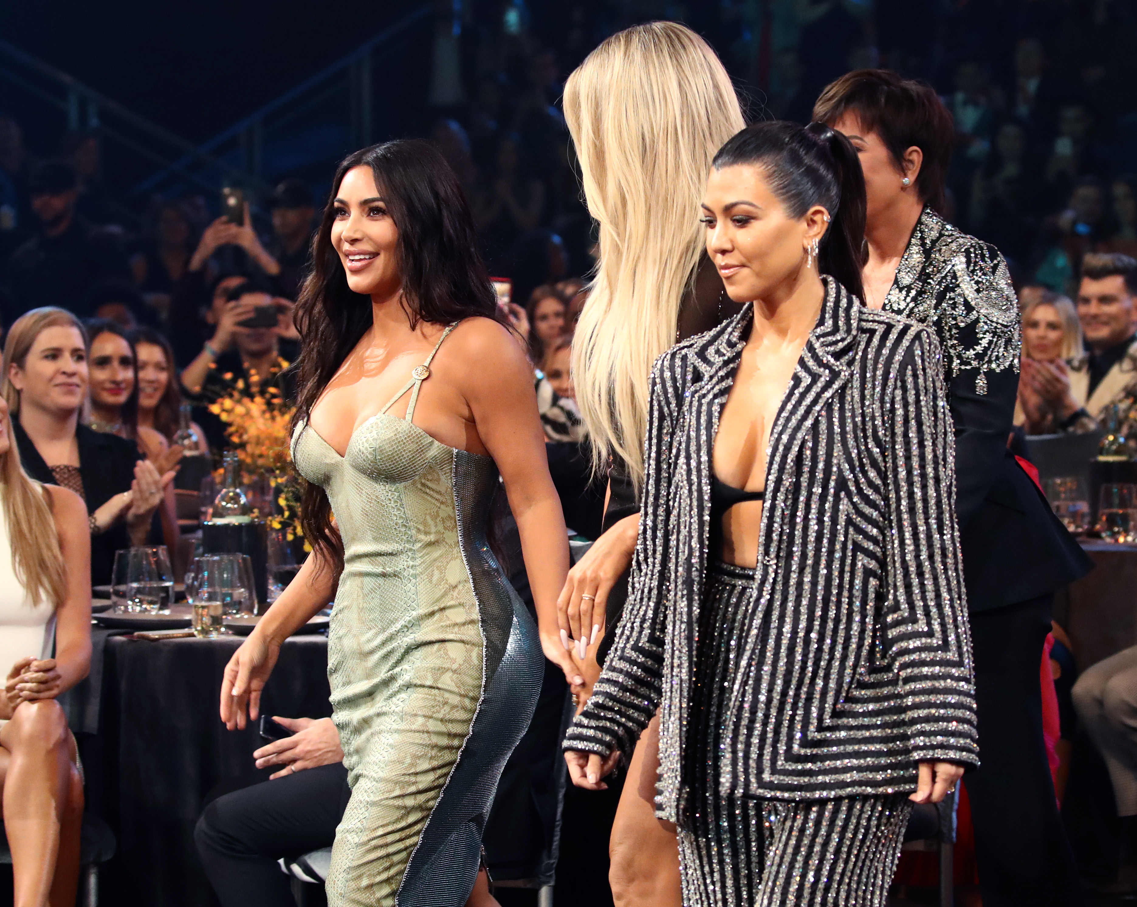 Kim Kardashian in a metallic dress and Kourtney Kardashian in a pinstriped suit at an event