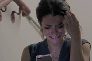Woman crying while looking at her phone, displaying emotional distress