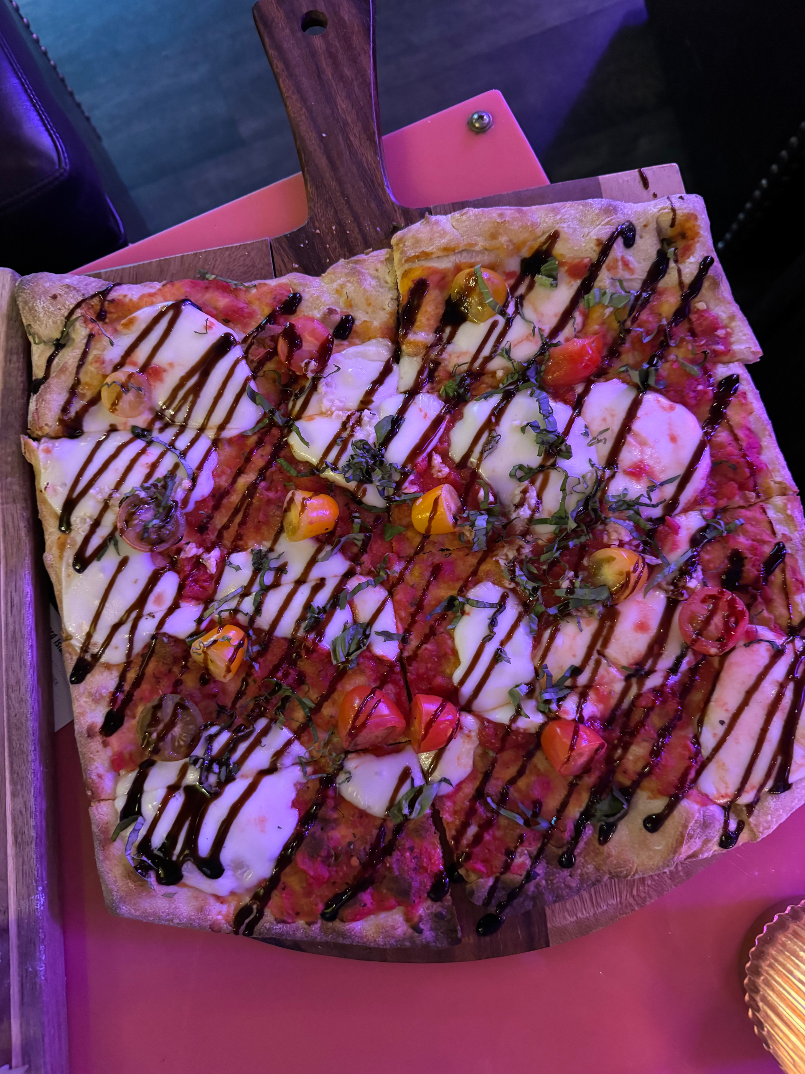 Flatbread pizza with drizzled sauce and assorted toppings on a wooden board