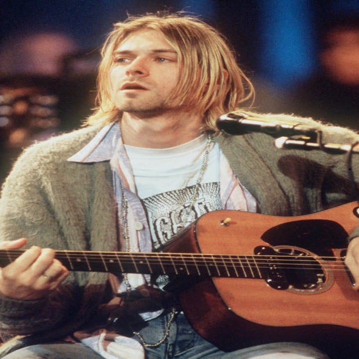 Kurt Cobain playing an acoustic guitar on stage, wearing a cardigan over a T-shirt